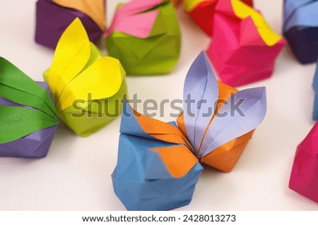 Angled view of two small origami rabbits propped against each other as if "kissing", surrounded by other bunnies, against a white backdrop.