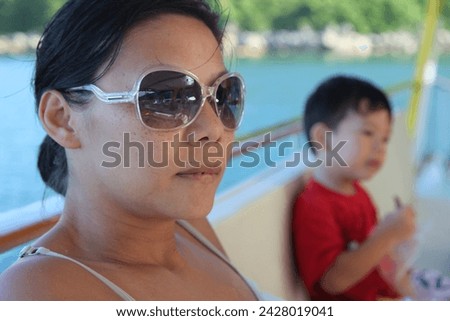 Exterior family portrait photo visual view of a beautiful woman mothe mom with her cute adorable young kid child children male boy on a boat having fun happy moment together in a relaxing day on boat