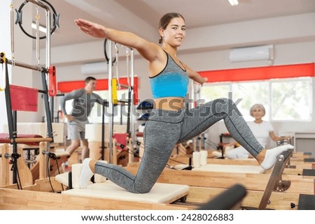 Young woman in sportswear training stretching using pilates machine in fitness studio..