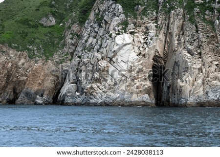 Exterior photo visual view of a natural nature ocean sea landscape with rocks island and caves with hill forest mountain on it in day time during summer nice isolated wild space with nobody on coast