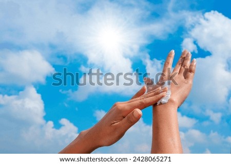 A woman is applying sunscreen and skin care to protect her skin from UV rays. She is applying sunscreen on her hand and arm. The sun symbol is a very sunny background. Health and skin care concept Royalty-Free Stock Photo #2428065271