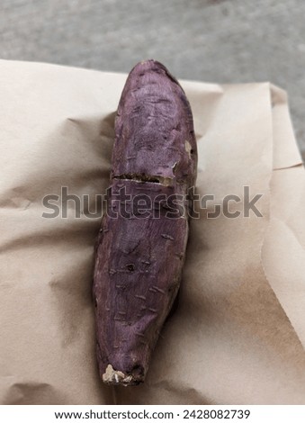 A purple sweet potato on a brown paper. The picture shows a purple sweet potato resting on a piece of brown paper or bag. The sweet potato has a deep purple skin, is elongated, and appears.