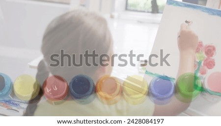 Image of paint pots over caucasian schoolgirl painting in art class. Creativity, school, education, childhood and learning, digitally generated image.