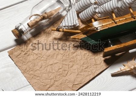 Message scroll letter in the bottle, sea ship and blank crumpled blank paper sheet with copy space on the white wooden desk table flat lay background. Ancient map concept.