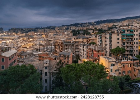 Genoa, Italy - Oct 04, 2023: Twilight panoramic cityscape with illuminated residential district on hillside under dark cloudy sky