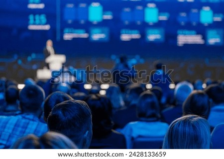 Professional conference with speaker presenting to an audience in a seminar hall, focus on crowd listening. Royalty-Free Stock Photo #2428133659
