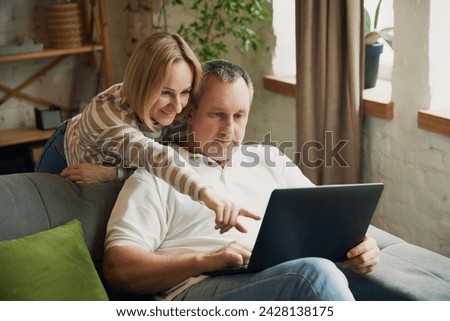 Husband and wife looking at laptop in the room. Woman pointing at screen. Middle aged couple shopping online together. Concept of fall in love, family, relationship, togetherness.