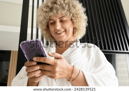Woman in a White Bathrobe Delightfully Engages With Her Smartphone. The Image Evokes Feelings of Leisure, Connectivity, And The Joy of Digital Communication.