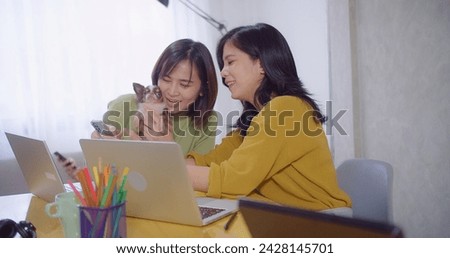 Two women enjoy a work break with a Chihuahua dog while discussing analyzes data business work on laptop screen at workspace desk home office