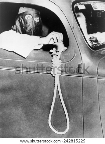Masked Ku Klux Klan member, holds a noose outside a car window during a parade through an African American neighborhood of Miami on the night before a primary election in May 1939. Royalty-Free Stock Photo #242815225