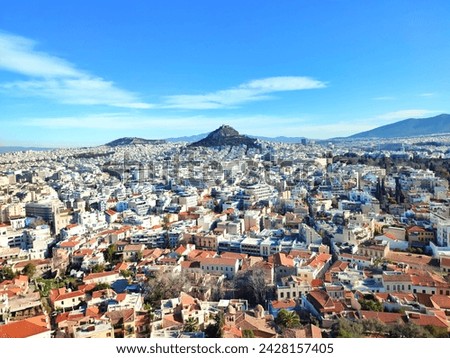 A panoramic view of Athens, Greece, with Mount Lycabettus clearly visible in the horizon. The colorful houses at the bottom of the image represent the picturesque Anafiotika neighborhood.