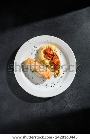 Top view of salmon steak with hummus and tomatoes on a white plate.