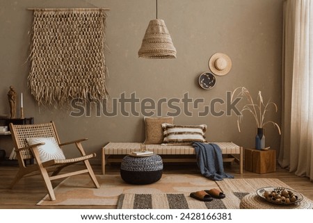 Interior design of ethno style living room with rattan furniture, daybed, pouf, hanging decoration on the wall, lamp and elegant personal accessories. Home decor. Template. Royalty-Free Stock Photo #2428166381