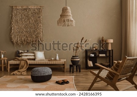 Interior design of ethno style living room with rattan furniture, daybed, pouf, hanging decoration on the wall, lamp and elegant personal accessories. Home decor. Template. Royalty-Free Stock Photo #2428166395