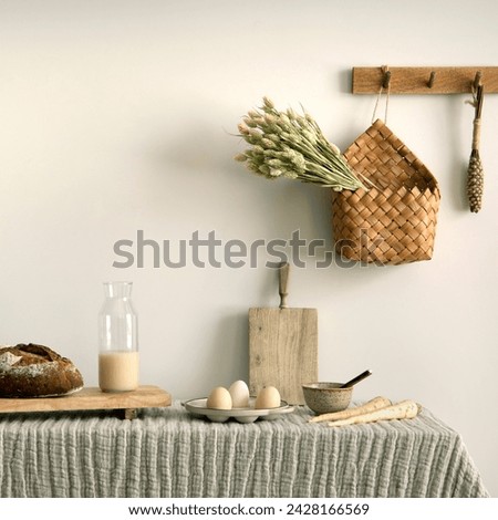 Interior design of kitchen space with rattan commode, cutting board, hanger, stylish tablecloth, basket with dried herbs, vegetables, food, bread, milk and kitchen accessories. Home decor. Template. 
