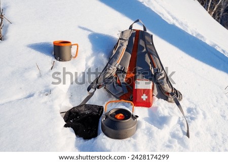 A first aid kit complements a tourist's equipment on a winter hike, camping in nature in the forest, dishes in the snow, a backpack for things. High quality photo