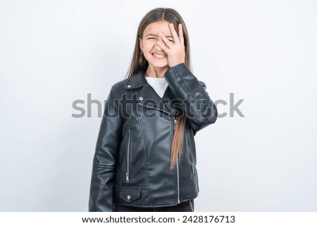 Young beautiful teen girl wearing biker jacket makes face palm and smiles broadly, giggles positively hears funny joke poses