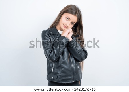 Charming serious Young beautiful teen girl wearing biker jacket  keeps hands near face smiles tenderly at camera