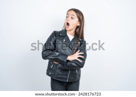 Shocked embarrassed Young beautiful teen girl wearing biker jacket keeps mouth widely opened. Hears unbelievable novelty stares in stupor