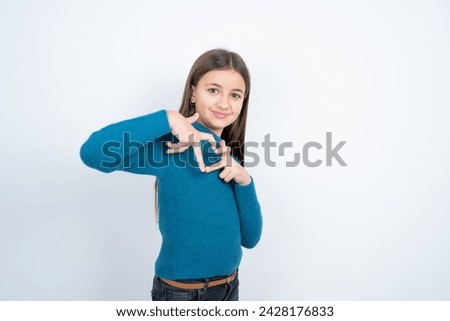 beautiful kid girl wearing blue knitted sweater smiling in love doing heart symbol shape with hands. Romantic concept.