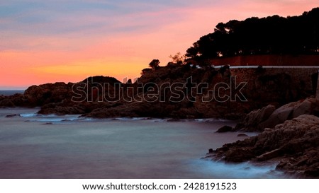 Spanish sunset on the cliff edge of S'Agaro. Long shutter speed creating flow of the waves crashing over the rocks as the sun casts an orange glow over the landscape.