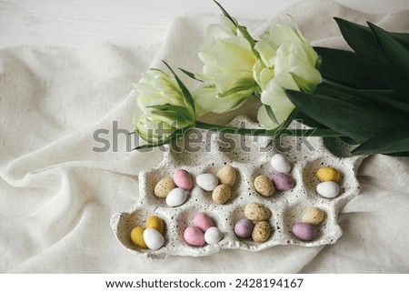 Happy Easter! Stylish easter eggs in tray and tulips on rustic table flat lay. Natural candy chocolate eggs with spring flowers. Easter hunt, space for text