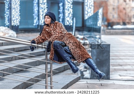 A stylish young woman in a leopard print fur coat and on the street of the city during the Christmas holidays.