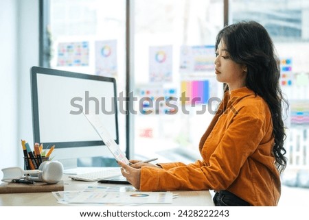 Side view of young creative woman using graphic tablet, working with color swatch samples on computer screen at workstation.