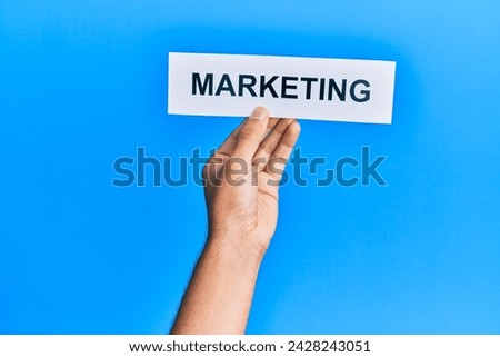 Hand of caucasian man holding paper with marketing word over isolated blue background