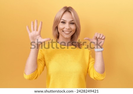 Young caucasian woman wearing yellow sweater showing and pointing up with fingers number six while smiling confident and happy. 