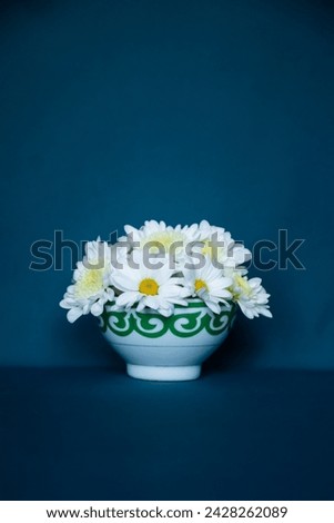 Kazakh traditional bowl — piala with national ornament filled with blooming camomille flowers. Pefrect photo for Nauryz greetings on dark blue background Royalty-Free Stock Photo #2428262089