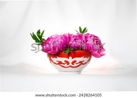 Kazakh piala. Central Asia traditional tea cup with national ornament filled with pink peonies. National red bowl isolated on white background Royalty-Free Stock Photo #2428264105