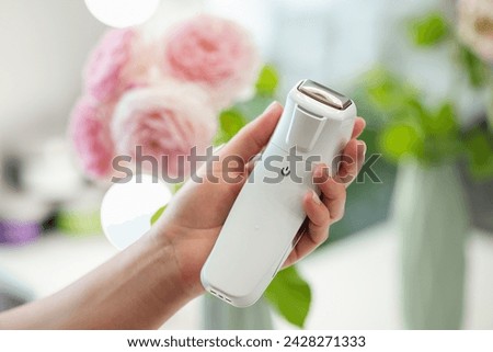 Tool for facial massage in hand of a professional cosmetologist, close up, flowers on the background. Professional device for body and skin care concept