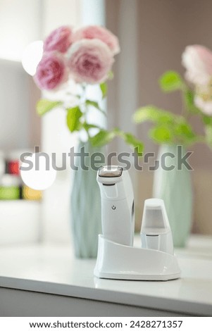 Devices for ultrasonic facial cleansing and massage standing on the table, close up. Mirror and beautiful rose flowers on the background in the beauty salon