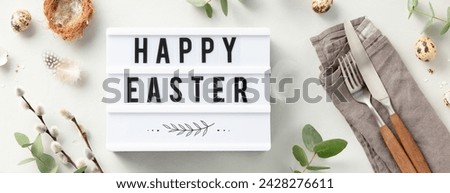 Easter table decorations. Stylish Easter brunch table setting with lightbox text Happy Easter, eggs, vintage cutlery, nests and spring branches on light grey background top view flat lay