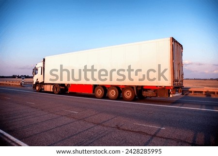 A truck with a refrigerated semi-trailer transports perishable food products in the evening against a blue sky. Import substitution, delivery of medicines. Royalty-Free Stock Photo #2428285995