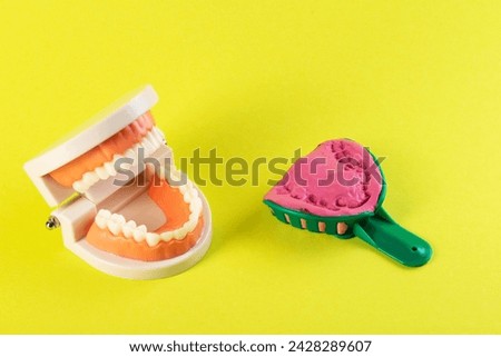 Green dental spoon for taking a dental impression in a mock-up of a dental jaw on a yellow background. Making an artificial jaw for malocclusion. Manufacturing of dental prostheses Royalty-Free Stock Photo #2428289607