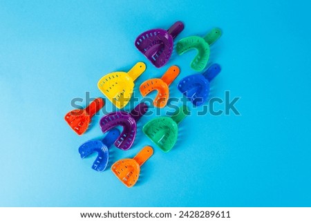 Multi-colored dental spoons for taking an impression of the dental jaw on a blue background. Orthodontics in dentistry. Dental prosthetics and crown manufacturing. Copy space for text Royalty-Free Stock Photo #2428289611