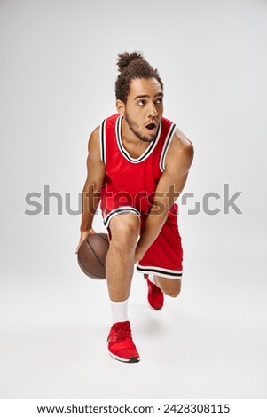 handsome sporty african american man in vibrant uniform playing basketball on gray background
