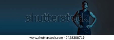 athletic african american man in sportwear with arms akimbo on dark lighted background, banner Royalty-Free Stock Photo #2428308719