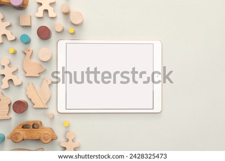 Modern tablet and wooden toys on light background, flat lay. Space for text