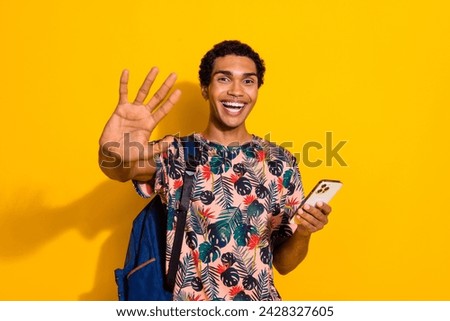 Photo of young man in t shirt in t shirt college or university with backpack using phone give highfive isolated on yellow color background
