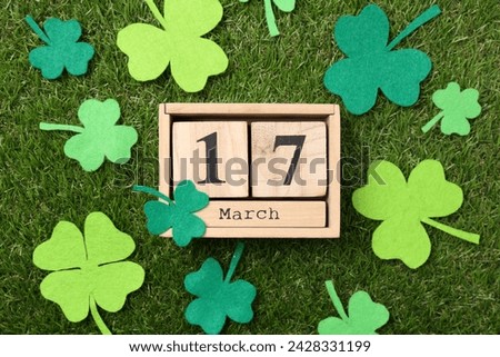 St. Patrick's day - 17th of March. Wooden block calendar and felt clover leaves on green grass, flat lay