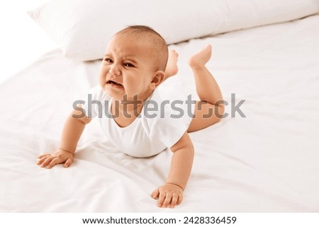 Beautiful little girl, child in white clothes lying on bed and crying against white background. Communication. Concept of childhood, family, care, motherhood, infancy, heath Royalty-Free Stock Photo #2428336459