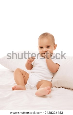 Portrait of beautiful little baby girl, toddler in onesie posing on bed against white background. Healthcare and education. Concept of childhood, family, care, motherhood, infancy, heath Royalty-Free Stock Photo #2428336463