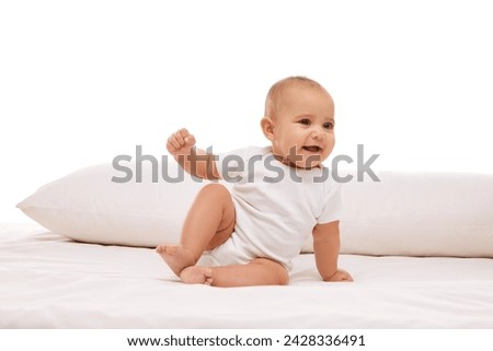 Little baby child, girl, infant in white onesie sitting on bed with pillow, smiling, making awkward moves against white background. Concept of childhood, family, care, motherhood, infancy, heath Royalty-Free Stock Photo #2428336491