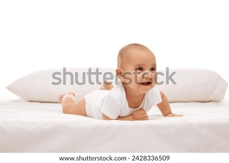 Beautiful baby, little girl in white comfortable clothes lying on belly on bed with pillow behind against white background. Happiness. Concept of childhood, family, care, motherhood, infancy, heath Royalty-Free Stock Photo #2428336509