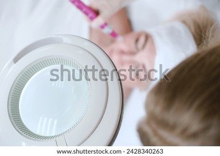 Overhead view of an esthetician using a dermapen on a client's face during a skin care procedure, focusing on the tool and treatment area. Horizontal photo