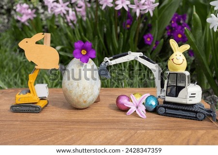model of a toy excavator, large and small multi-colored Easter eggs on a background of spring blooming flowers. Easter spring holiday concept for construction companies. Business card