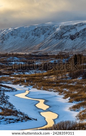 A small stream meanders half-frozen through the lava and landscape of southern Iceland. In the background is the mountain Ingólfsfjall Royalty-Free Stock Photo #2428359311